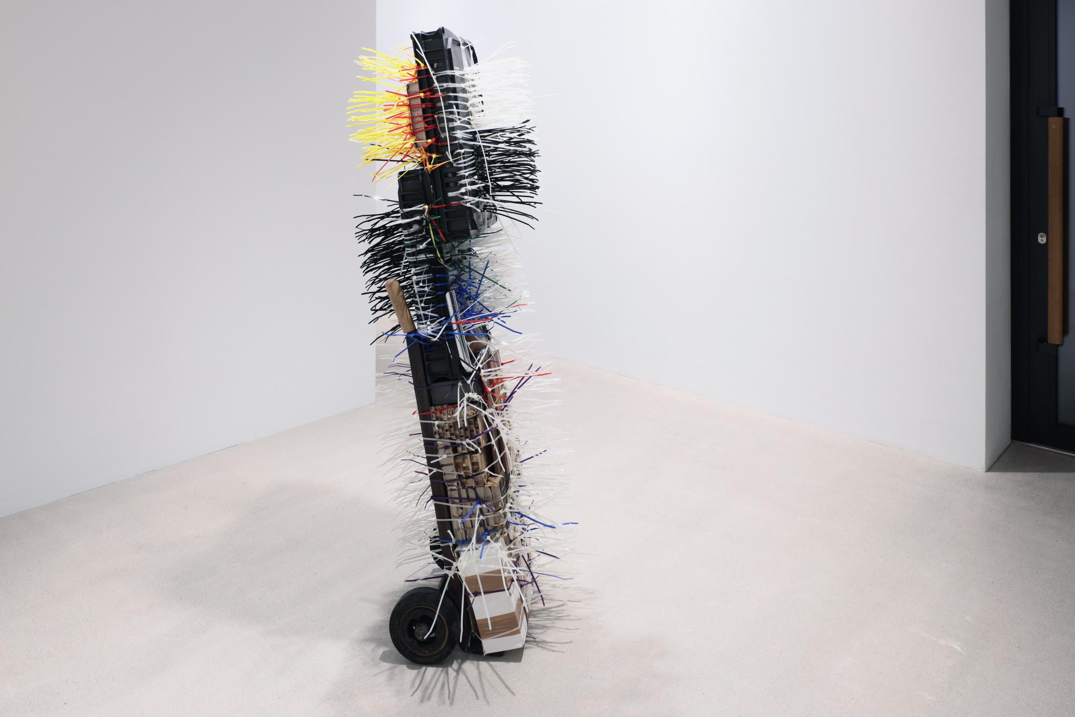 Exhibition View Umut Yasat Solo Show «35; view on Umut Yasat, Der Stapel 84, 2022, 175 x 58 x 72 cm, wood, plastic, steel, iron, ink, pencil, felt-tip pen, glue, tobacco, stainless steel, copper, cardboard, soil, aluminum, cotton, lime, water, whiskey, carbon dioxide, sugar, brass, E150d, E338, caffeine, silver, gold, tin, lithium, glass» at Windhager von Kaenel, Zurich, 2022 / Courtesy: the artist and Windhager von Kaenel