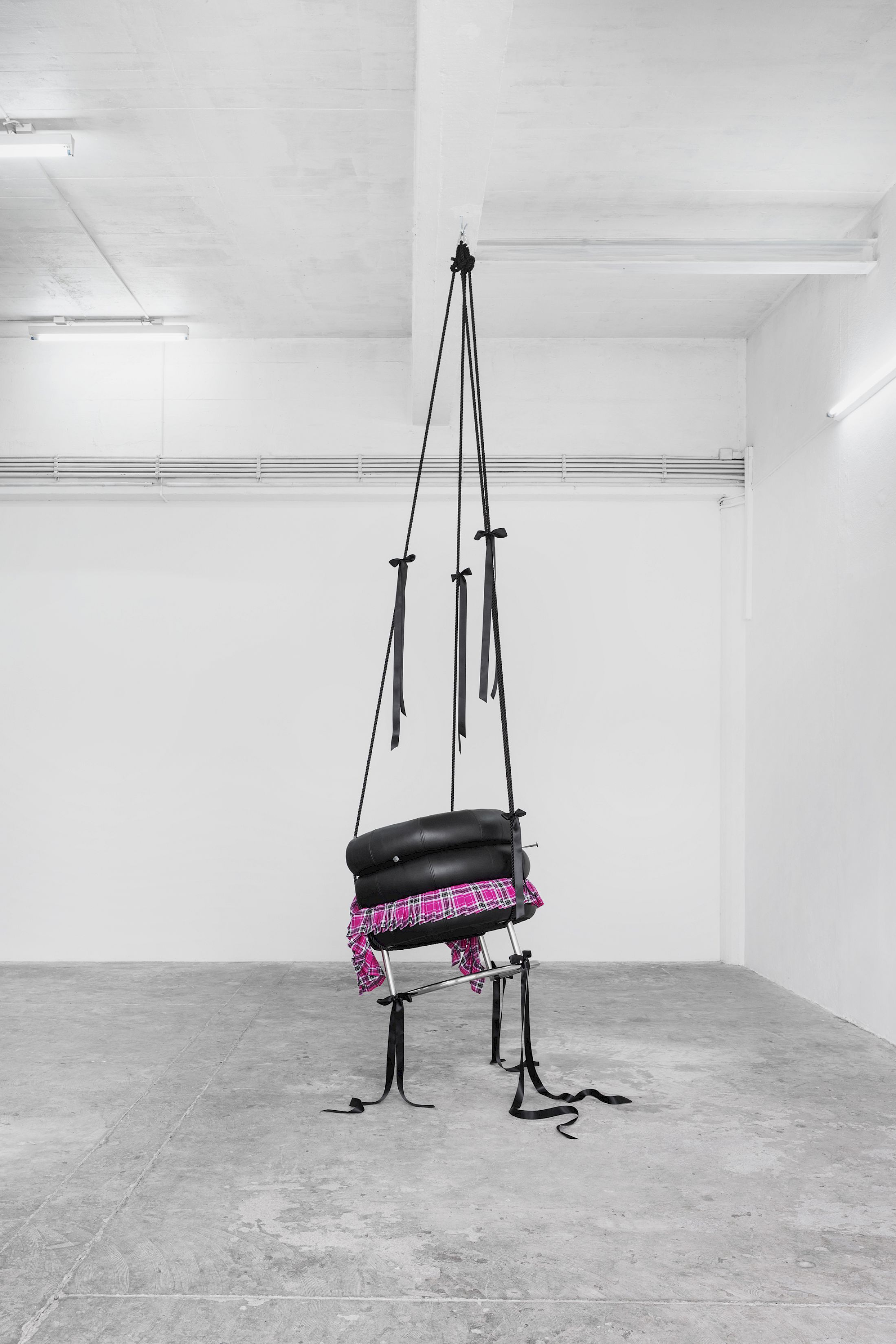 Exhibition View Solo Show Lauryn Youden «I wanna hold the hand inside you ; view on Would you die tonight for love?, 2025, Bibendum Chair (1926), pink plaid skirt, black ribbons, black mooring line, heart locket necklace with red hair, 3x handforged nails, 370 × 93 × 77 cm (suspended)» at CIRCUIT, Lausanne, 2025 / Photo: Aude Mayer / Courtesy: the artist and CIRCUIT