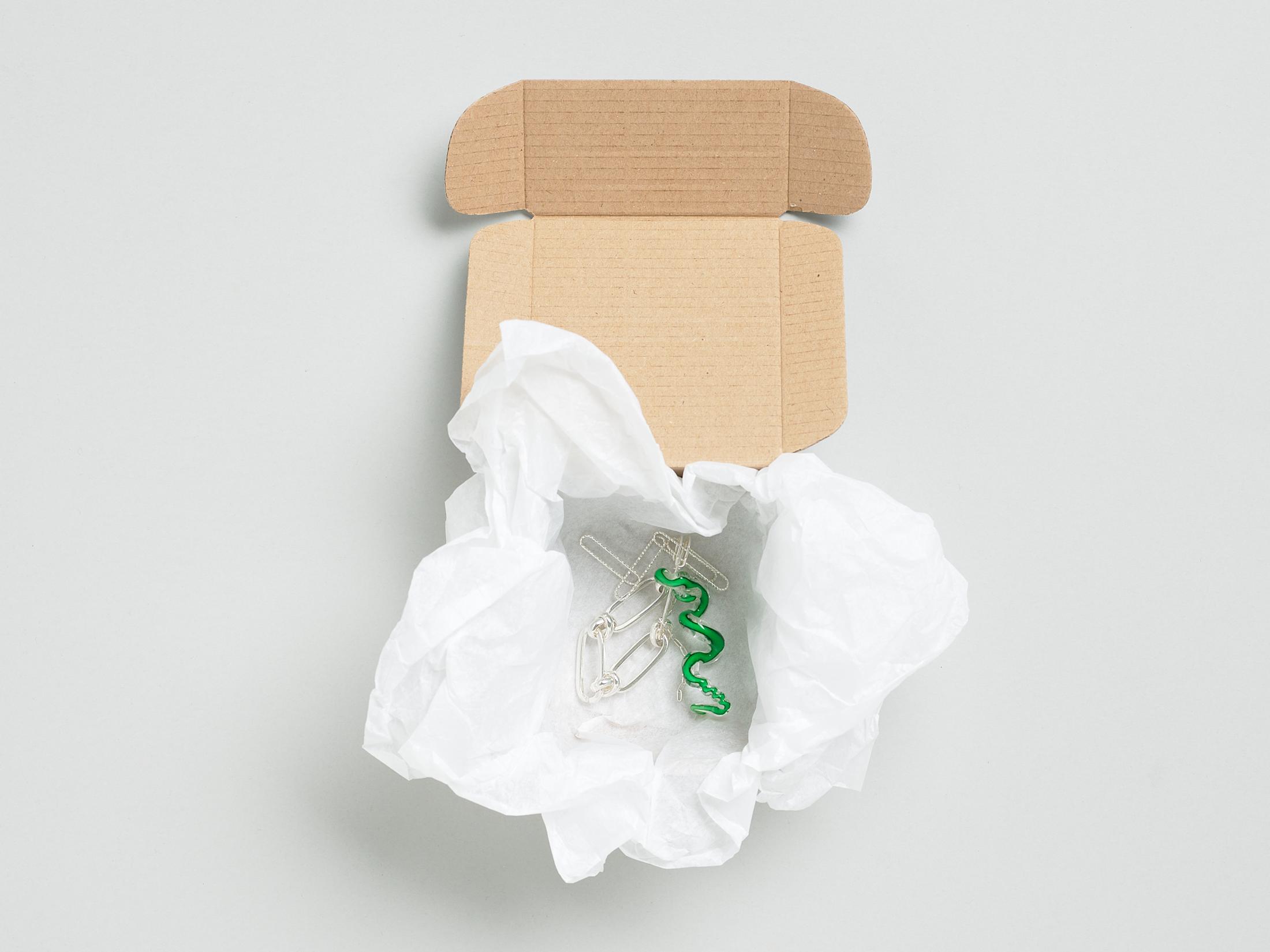 Exhibition View Solo Show Caroline Schattling Villeval «Carences et toute-puissance; view on Caroline  Schattling Villeval, No, no no healthy trust, 2023, A box containing a safety pin that joins together an object made of Murano glass and two or three silver-plated brass chains, wrapped in tissue paper (On the bottom of the box is printed a QR-code that gives access to the animation video, No, no no healthy trust, color, 2’, 2023), variable dimensions, black print on a white box, 9.2 x 9.2 x 5 cm» at Centre d'édition contemporaine, Geneva, 2024 / Photo: Sandra Pointet / Courtesy: the artist and Centre d'édition contemporaine, Geneva