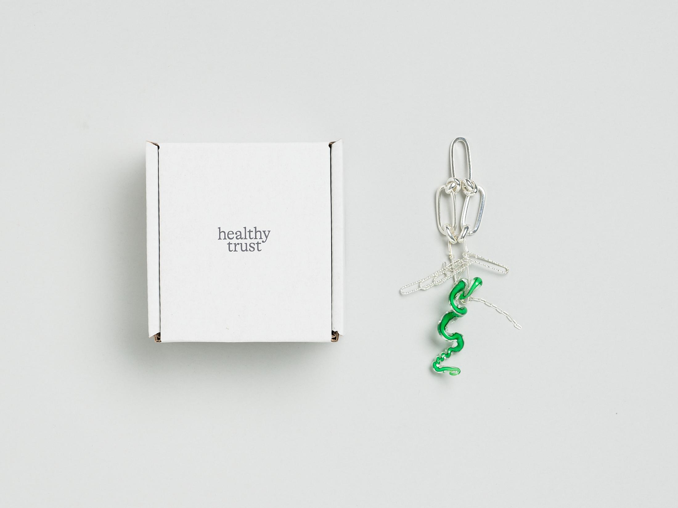 Exhibition View Solo Show Caroline Schattling Villeval «Carences et toute-puissance; view on Caroline  Schattling Villeval, No, no no healthy trust, 2023, A box containing a safety pin that joins together an object made of Murano glass and two or three silver-plated brass chains, wrapped in tissue paper (On the bottom of the box is printed a QR-code that gives access to the animation video, No, no no healthy trust, color, 2’, 2023), variable dimensions, black print on a white box, 9.2 x 9.2 x 5 cm» at Centre d'édition contemporaine, Geneva, 2024 / Photo: Sandra Pointet / Courtesy: the artist and Centre d'édition contemporaine, Geneva