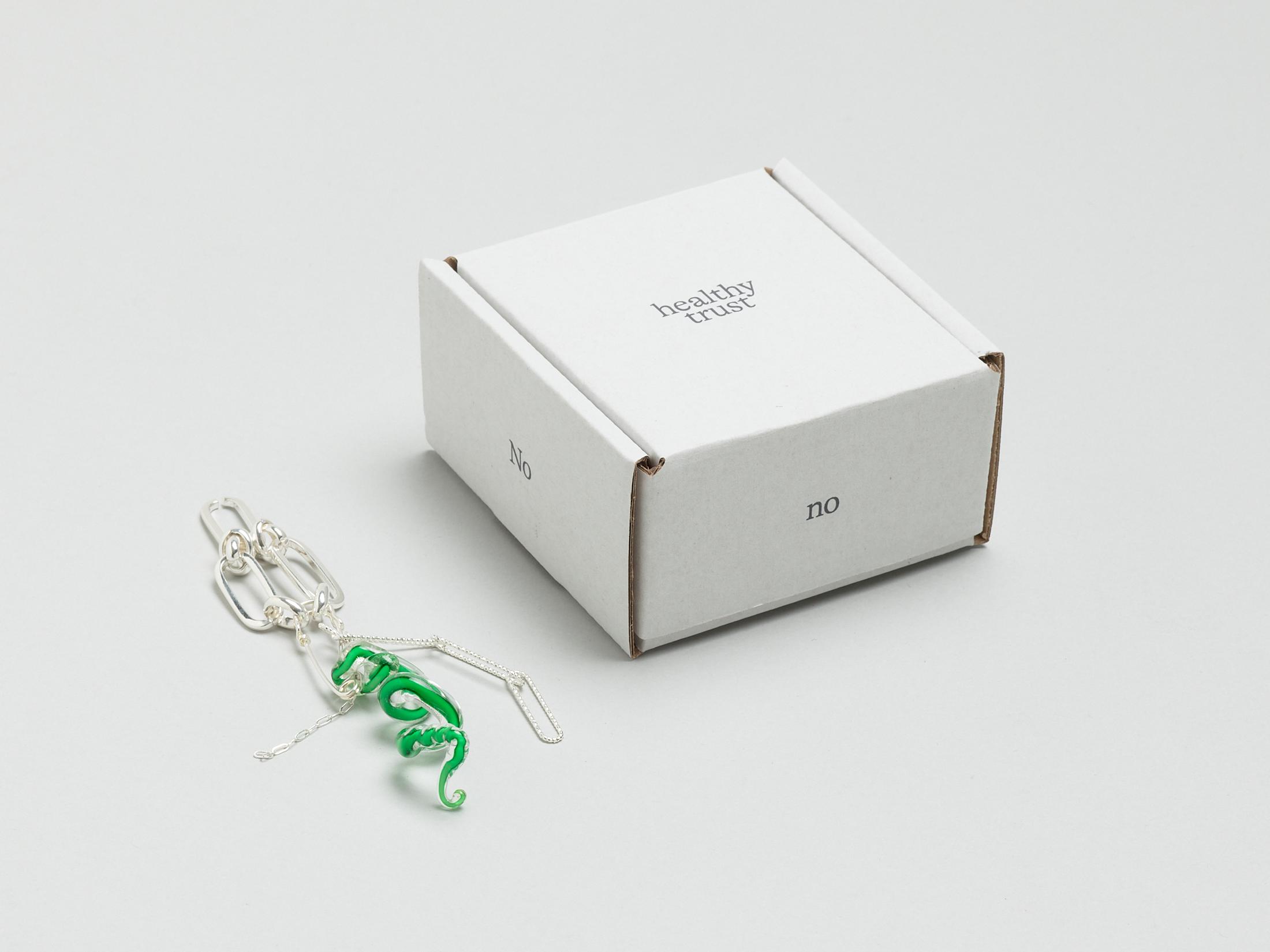 Exhibition View Solo Show Caroline Schattling Villeval «Carences et toute-puissance; view on Caroline  Schattling Villeval, No, no no healthy trust, 2023, A box containing a safety pin that joins together an object made of Murano glass and two or three silver-plated brass chains, wrapped in tissue paper (On the bottom of the box is printed a QR-code that gives access to the animation video, No, no no healthy trust, color, 2’, 2023), variable dimensions, black print on a white box, 9.2 x 9.2 x 5 cm» at Centre d'édition contemporaine, Geneva, 2024 / Photo: Sandra Pointet / Courtesy: the artist and Centre d'édition contemporaine, Geneva