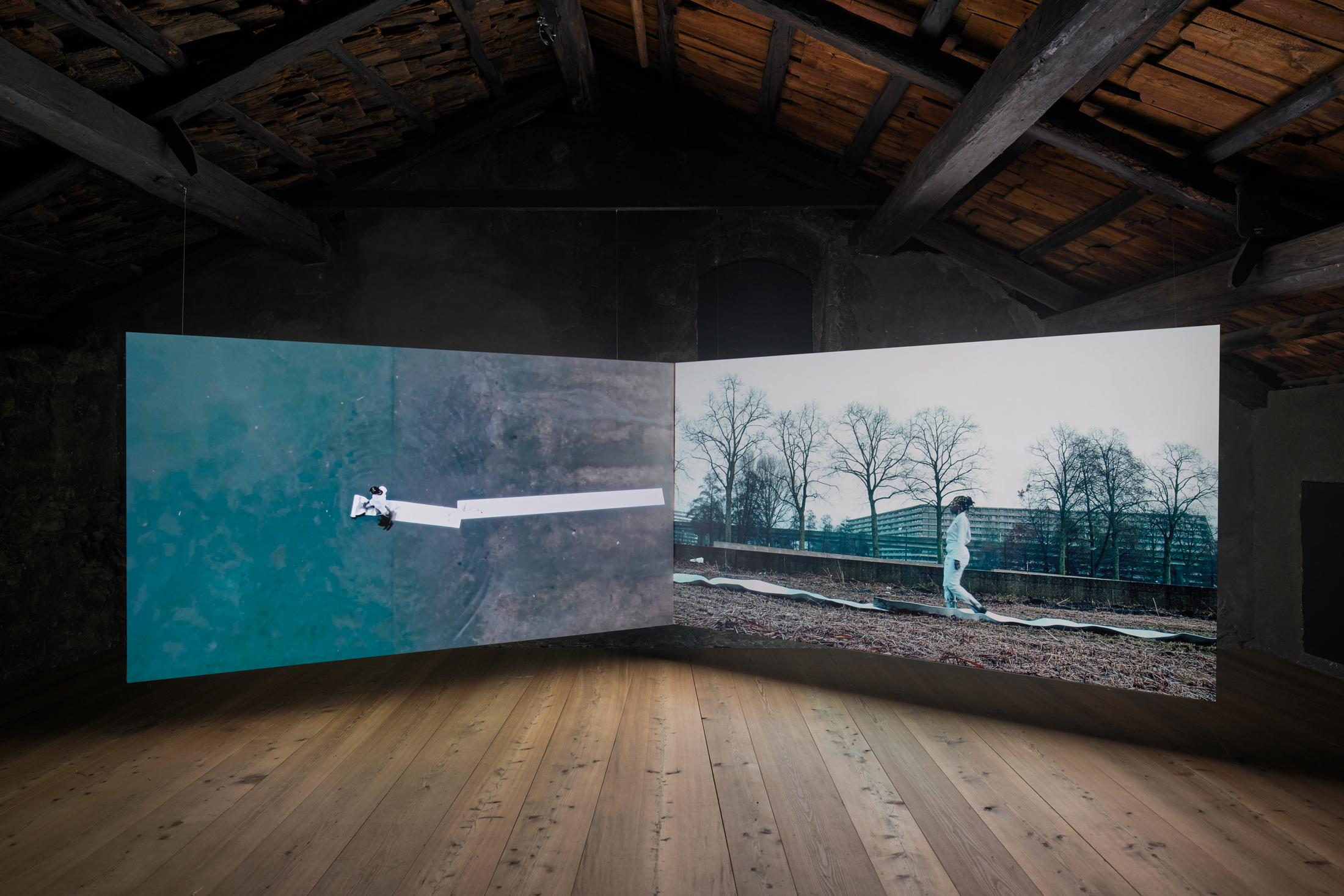 Exhibition View donna Kukama Solo Show «transcendence; view on donna Kukama, Chapter Q: Dem Short-Short falls, 2017 - 2018, Video double projection, Film Still, Part 1: 12 min 10 sec., Part 2: 12 min 11 sec» at Galerie Tschudi, Zuoz, 2023 / Photo: Ralph Feiner / Courtesy: the artist and Galerie Tschudi