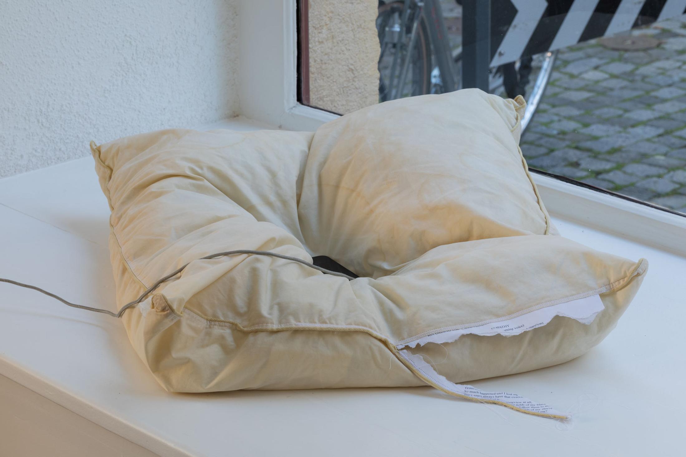 Exhibition View Leolie Greet with Amélie Bodenmann, Anina Müller and Nina Rieben Show «mumbles slide along the sleeve; view on Anina Müller & Leolie Greet, btw this is a message from Empathy, 2023, audio, iphone, cushion, stitched paper» at Krone Couronne, Biel, 2023 / Photo: Guadalupe Ruiz / Courtesy: the artists and Krone Couronne