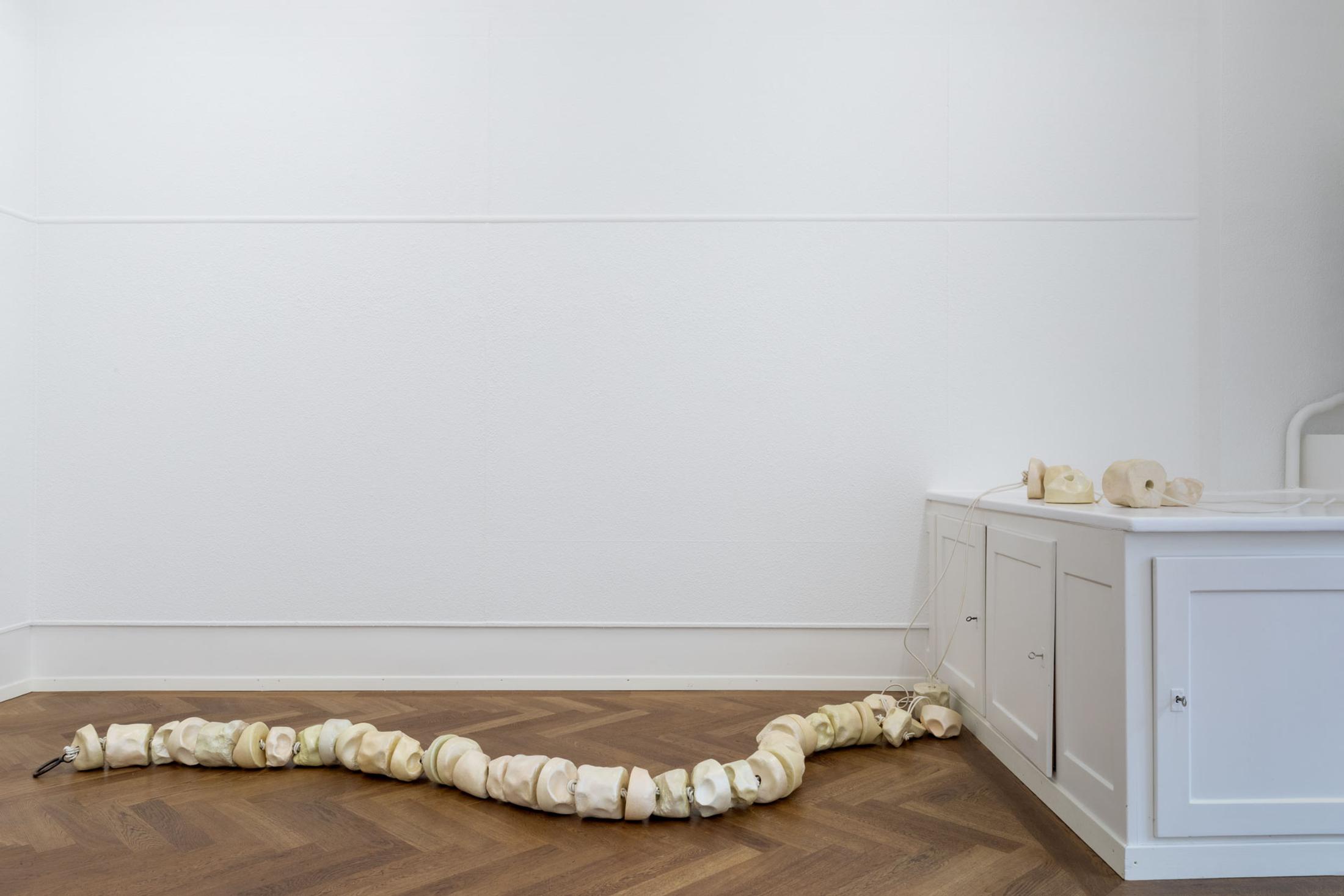 Exhibition View Leolie Greet with Amélie Bodenmann, Anina Müller and Nina Rieben Show «mumbles slide along the sleeve; view on Leolie Greet, THE TONGUE (licking words to pearls), 2023, plaster, gouache, varnish, pearlescent pigments, elastic thread, steel» at Krone Couronne, Biel, 2023 / Photo: Guadalupe Ruiz / Courtesy: the artist and Krone Couronne