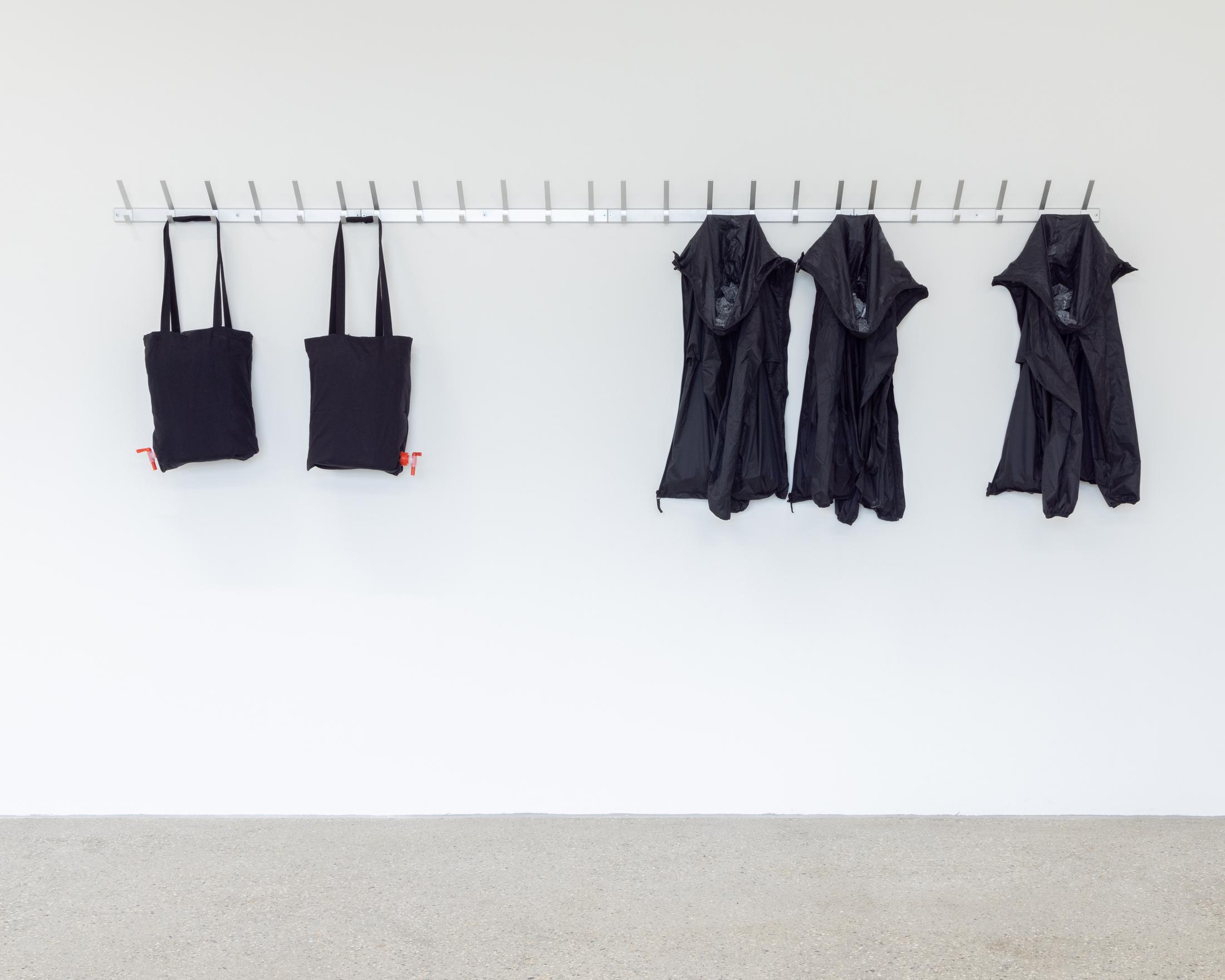 Exhibiton View Solo Show Shirin Yousefi «BAZM; view on BAZM (coat rack), 2024, wall-mounted coat rack, pilgrims, plastic drums and pebbles, dimensions variable» at CALM – Centre d’Art La Meute, Lausanne, 2024 / Photo: Théo Dufloo / Courtesy: the artist and CALM – Centre d’Art La Meute