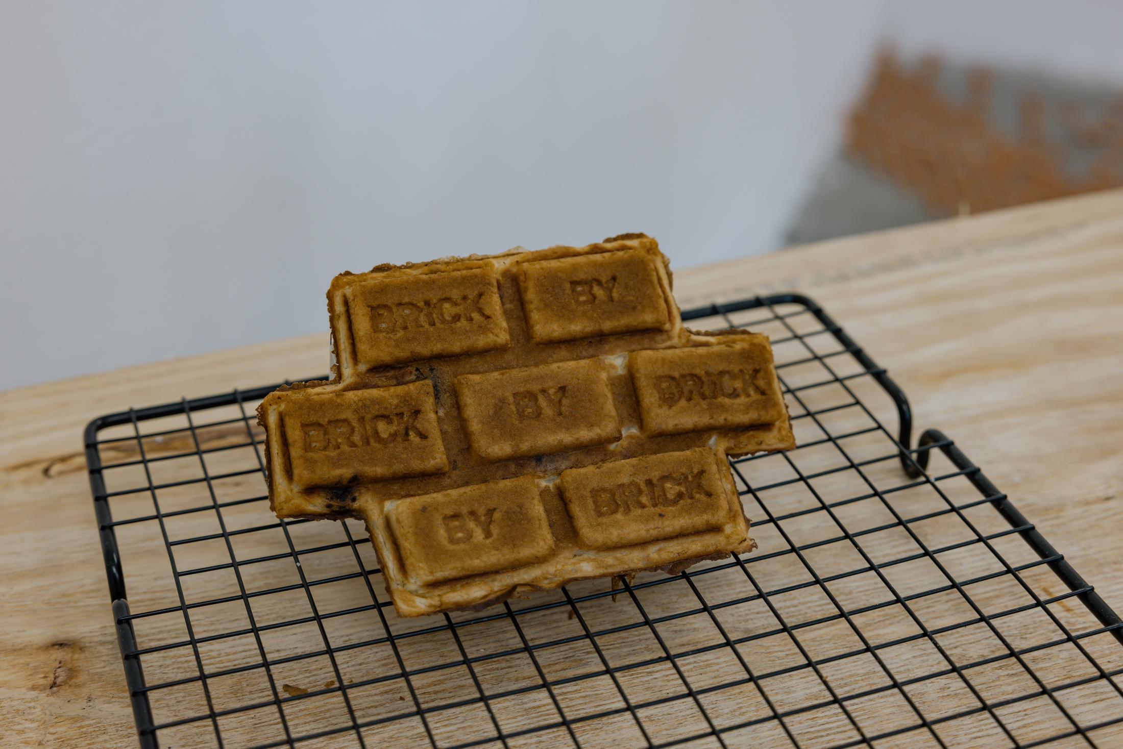Exhibition View Duo Show Stirnimann-Stojanovic «Connecting through Collective Care and Redistribution; view on Stirnimann-Stojanovic X SoliSoli, SoliSoliWaffle, Custom-made waffle machine (the waffles mimic a brick wall inscribed with “Brick by Brick” and “Wall by Wall”), 37.5 x 50 x 27 cm, 2024» at WallStreet Fribourg, Fribourg, 2025 / Photo: Julie Folly / Courtesy: the artists and WallStreet