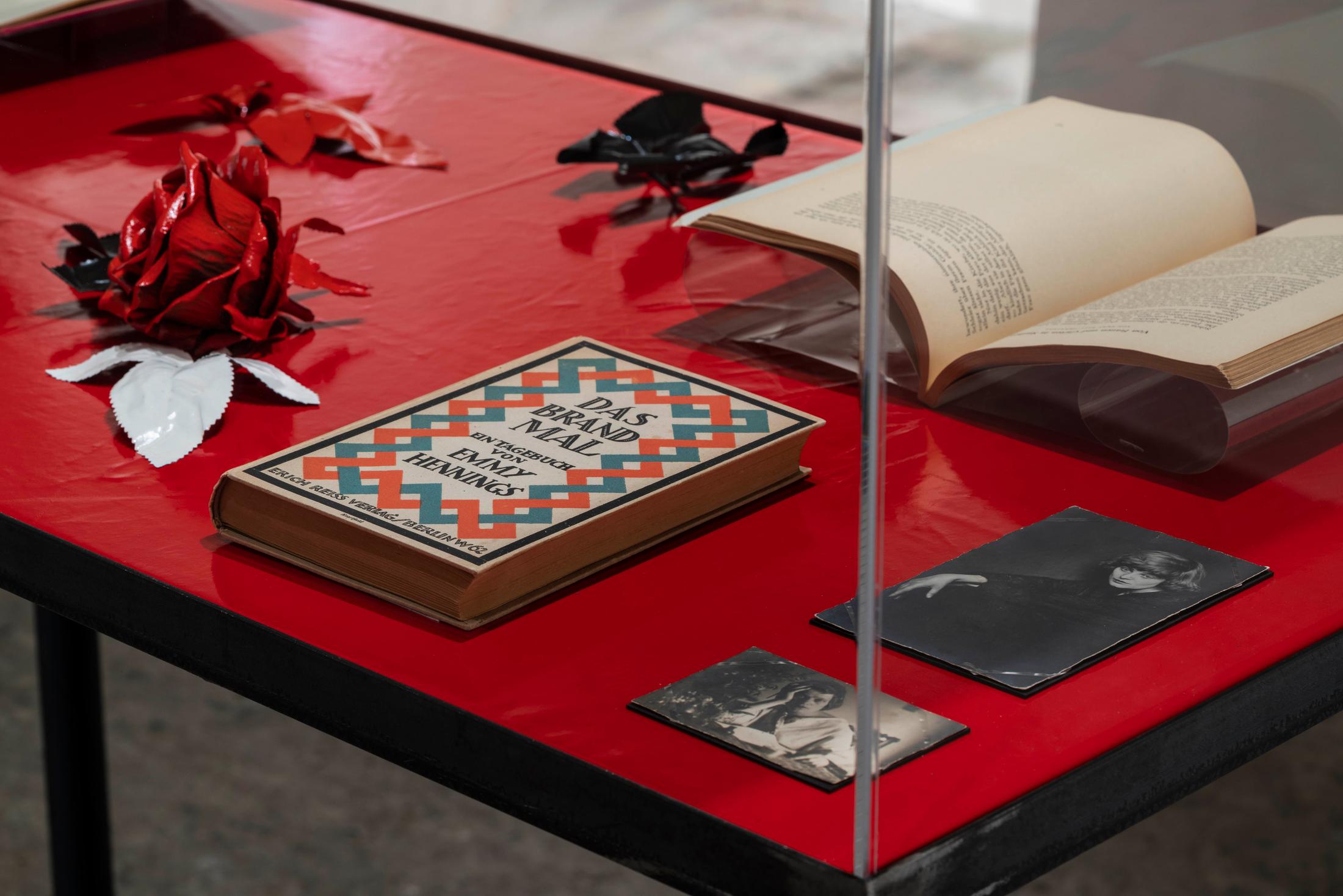 Exhibition View Emmy Hennings / Sitara Abuzar Ghaznawi Joint Exhibition (view on Sitara Abuzar Ghaznawi, Showcase (Traffic Red), 2020; Emmy Hennings, Das Brandmal. Ein Tagebuch (first edition of the novel), 1920; Emmy Hennings in Agnuzzo am Tisch sitzend, photography, approx. 1917/1918; Emmy Hennings von Hans Holdt porträtiert, photography, 1921–1922; Emmy Hennings, Von Gärten und Frauen in Sizilien, article, 1952) at Cabaret Voltaire, Zurich, 2020 / Photo: Gunnar Meier / Courtesy Sitara Abuzar Ghaznawi: the artist; Courtesy Emmy Hennings: Schweizerisches Literaturarchiv and Cabaret Voltaire