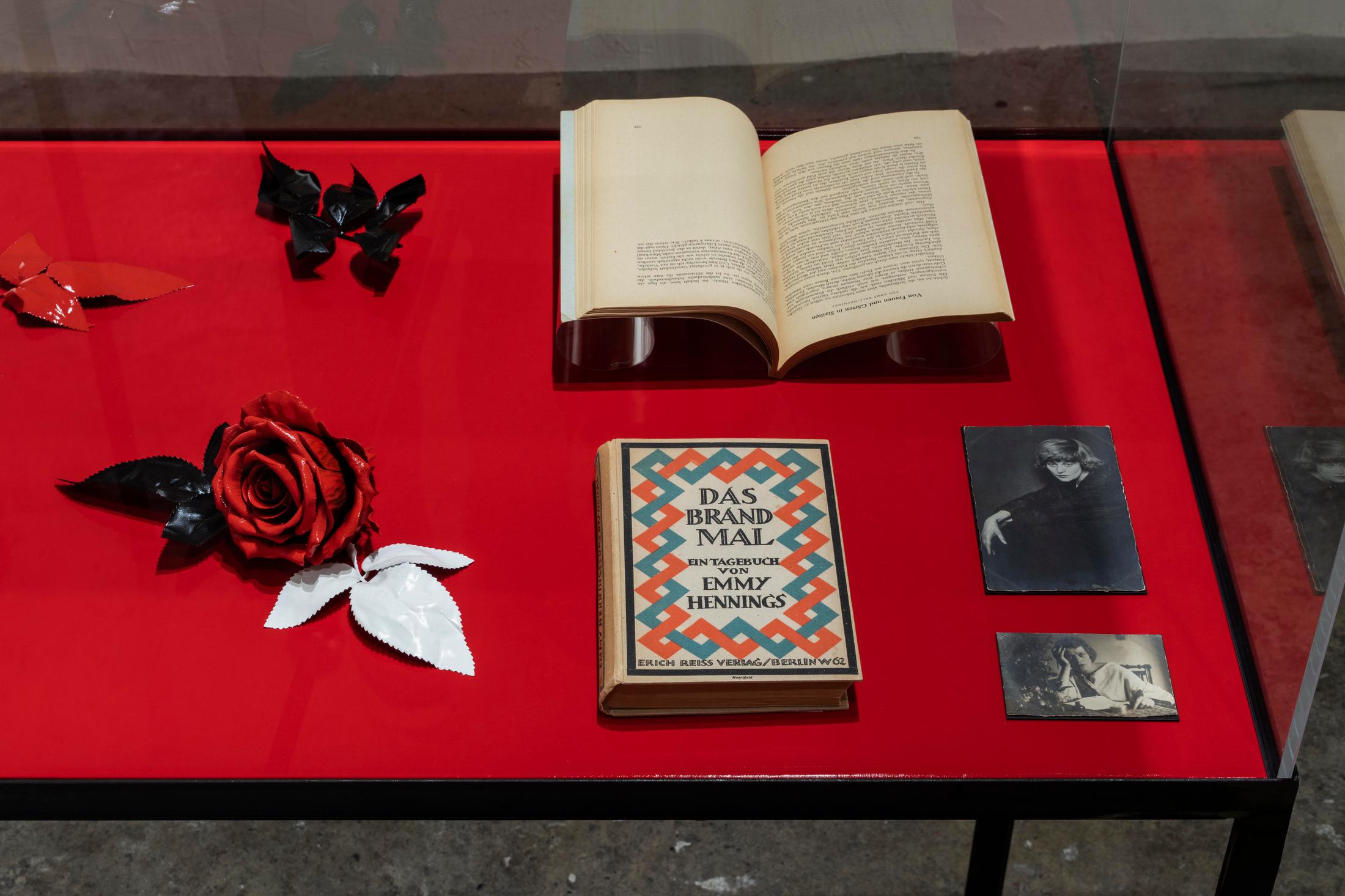 Exhibition View Emmy Hennings / Sitara Abuzar Ghaznawi Joint Exhibition (view on Sitara Abuzar Ghaznawi, Showcase (Traffic Red), 2020; Emmy Hennings, Das Brandmal. Ein Tagebuch (first edition of the novel), 1920; Emmy Hennings in Agnuzzo am Tisch sitzend, photography, approx. 1917/1918; Emmy Hennings von Hans Holdt porträtiert, photography, 1921–1922; Emmy Hennings, Von Gärten und Frauen in Sizilien, article, 1952) at Cabaret Voltaire, Zurich, 2020 / Photo: Gunnar Meier / Courtesy Sitara Abuzar Ghaznawi: the artist; Courtesy Emmy Hennings: Schweizerisches Literaturarchiv and Cabaret Voltaire