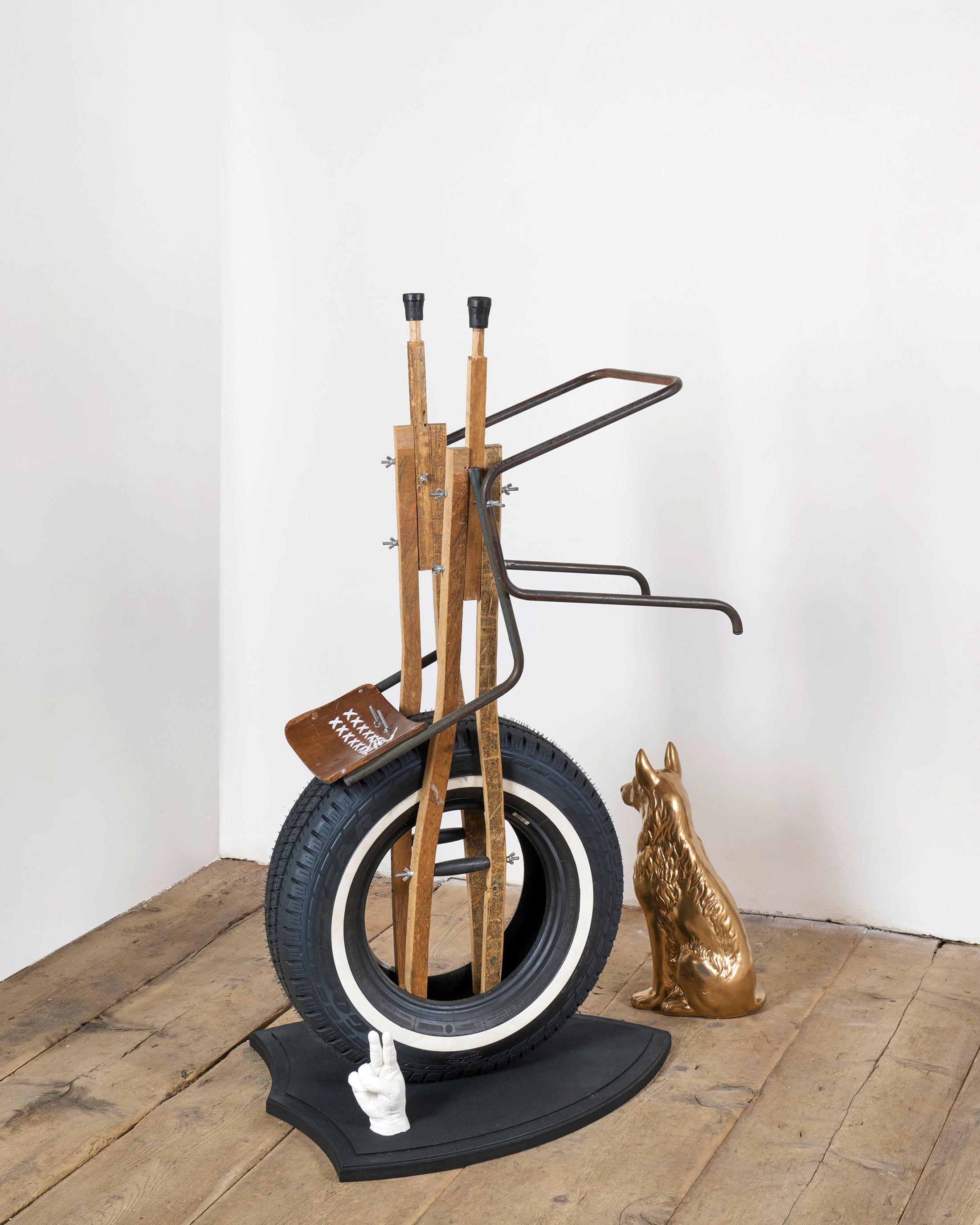 Exhibition View Kemang Wa Lehulere Solo Show «Where Did the Sky Go?; view on Kemang Wa Lehulere, The Conjunction 1, 2020, salvaged school chair, crutches from salvaged school desk, car tyre, wooden trophy shield, resin moulded hand, porcelain dog, shoe laces 146 x 65 x 84 cm and dog» at Galerie Tschudi, Zuoz, Engadin, 2020 / Photo: Ralph Feiner / Courtesy: the artist and Galerie Tschudi